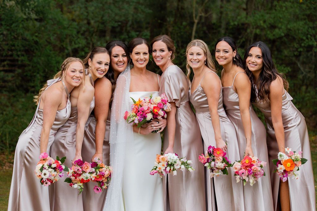 Bride and bridesmaids in champagne dresses holding pink and white bouquets outdoors in a garden