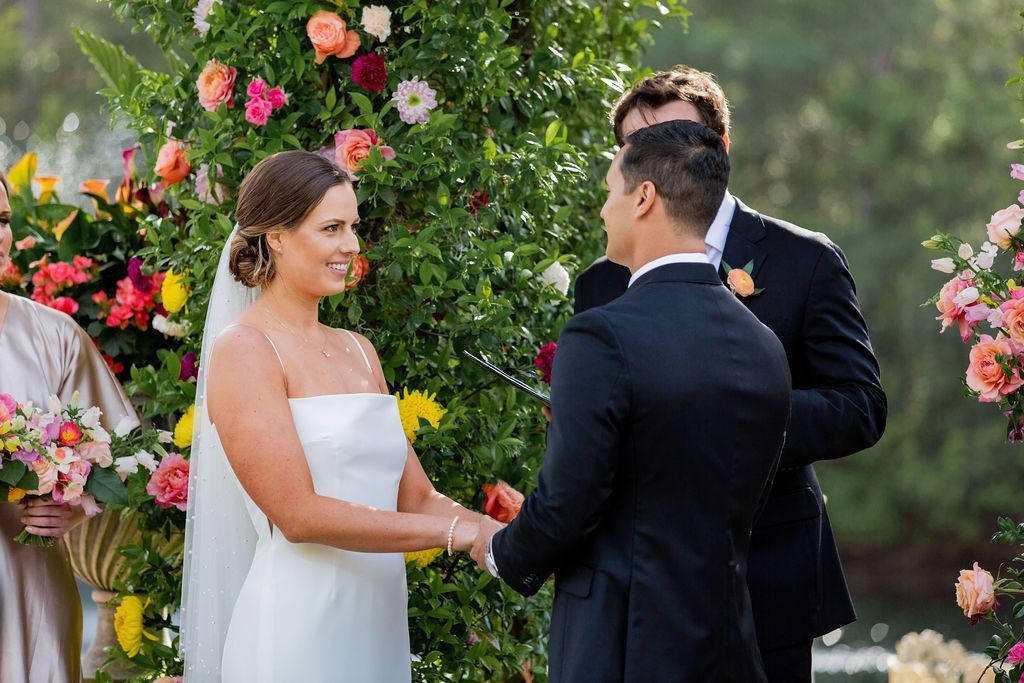 Bride and groom holding hands during an outdoor wedding ceremony among flowers