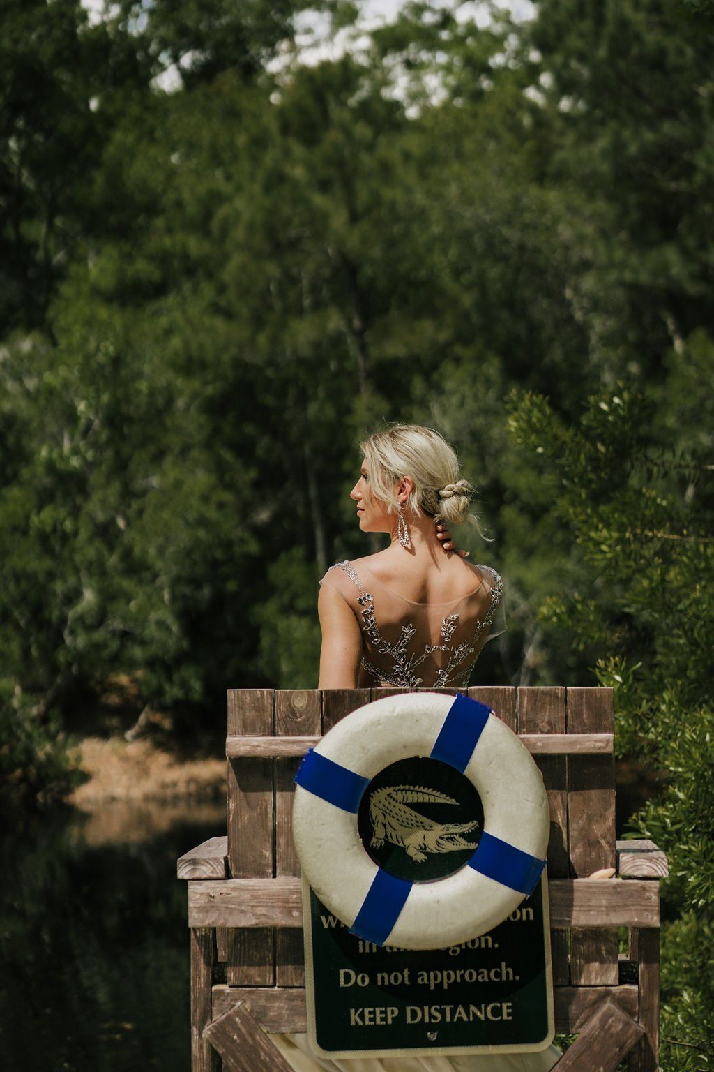 Person seen from behind in a wooden lifeguard-style seat with a life preserver, outdoors near trees.