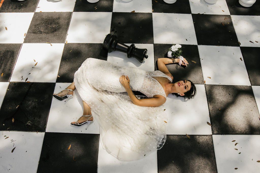Person in a white dress lying on a black-and-white checkered floor with flowers nearby