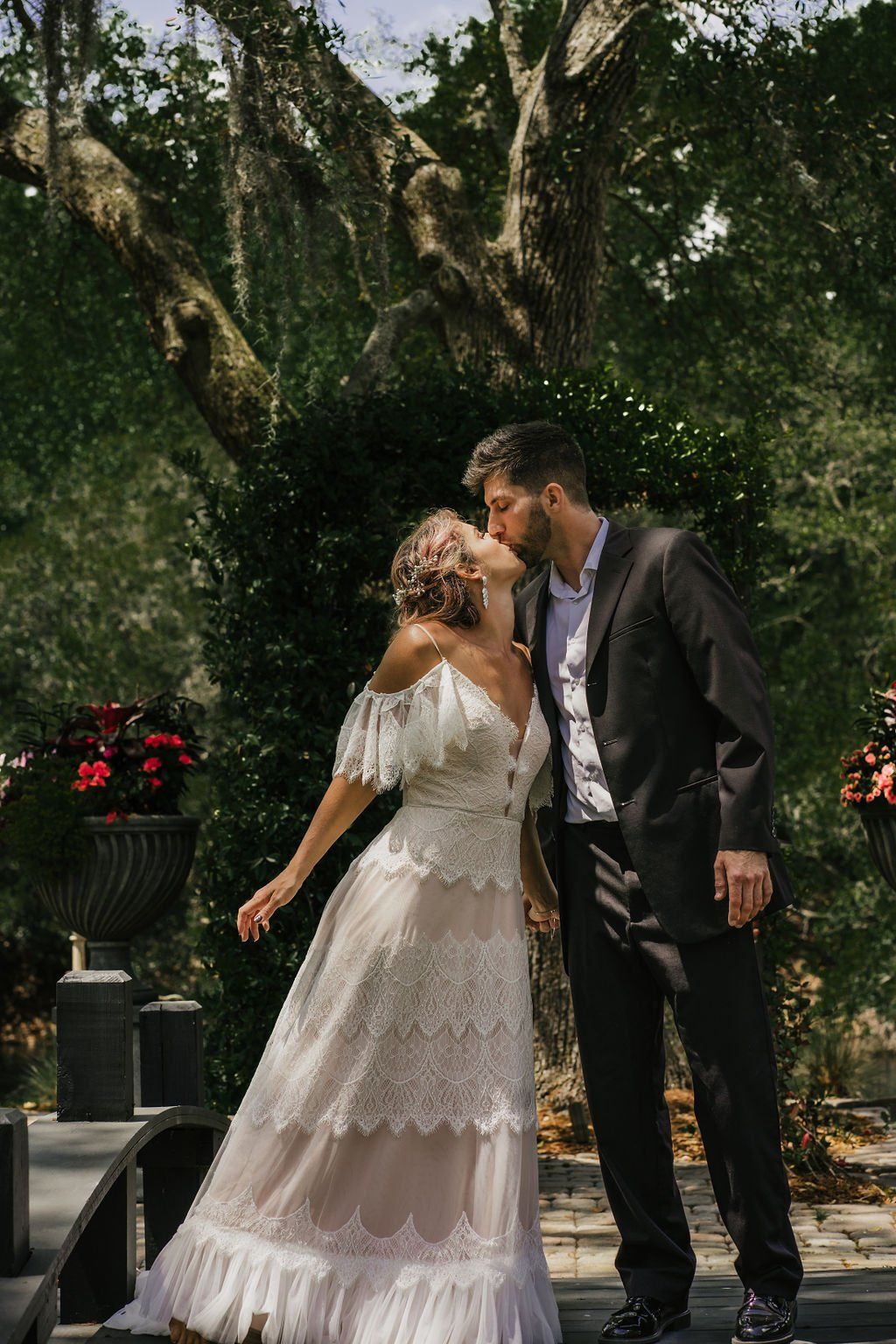 Couple kissing in formal attire in a garden beneath hanging greenery