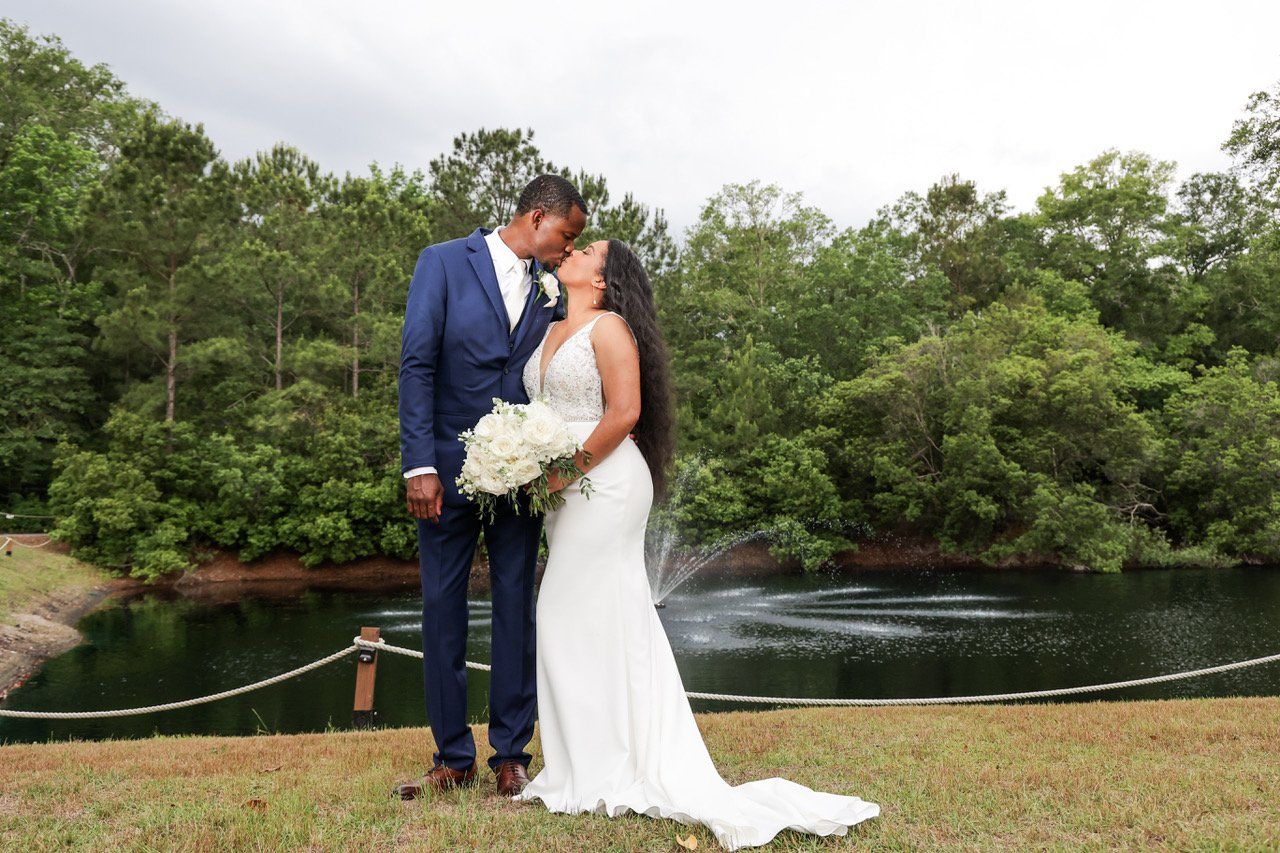 Couple in wedding attire kissing by a river with trees in the background