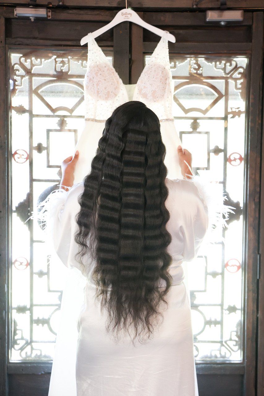 Woman in white holding a garment on a hanger, seen from behind in a bright doorway.