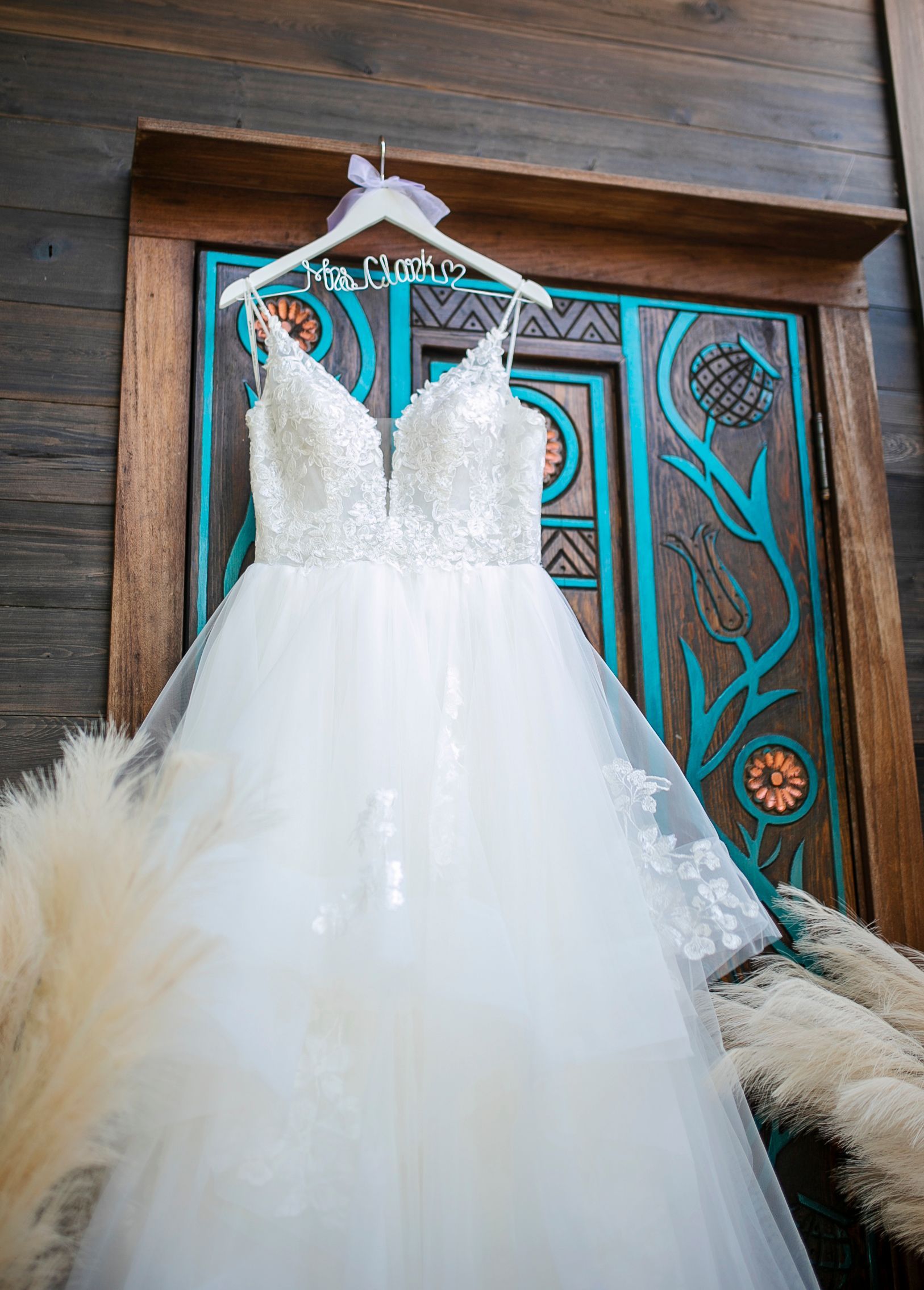 White lace wedding dress with a tulle skirt hanging in front of a carved wooden door with teal accents