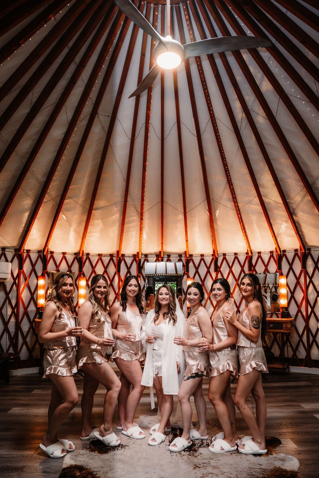 Group posing in matching tan outfits inside a yurt-like venue with warm lighting and patterned walls