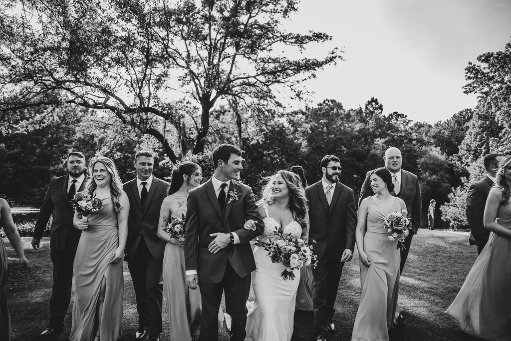Wedding party walking outdoors with bride and groom centered under trees
