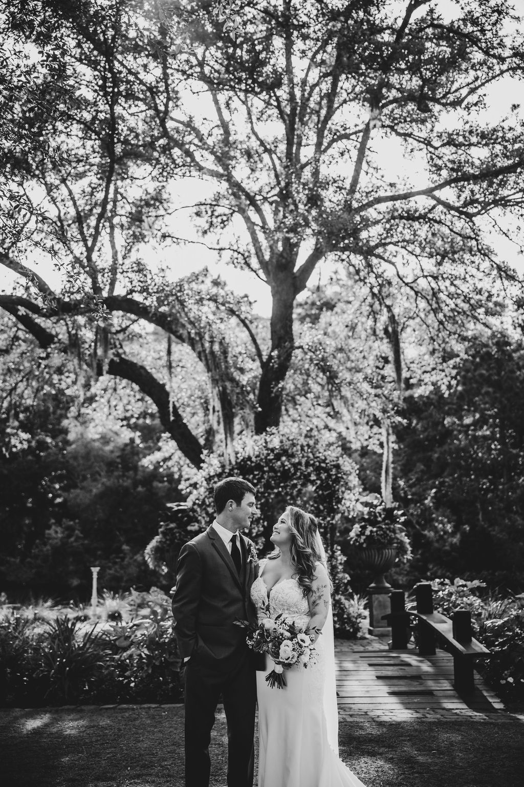 Bride and groom standing together in a garden beneath a large tree