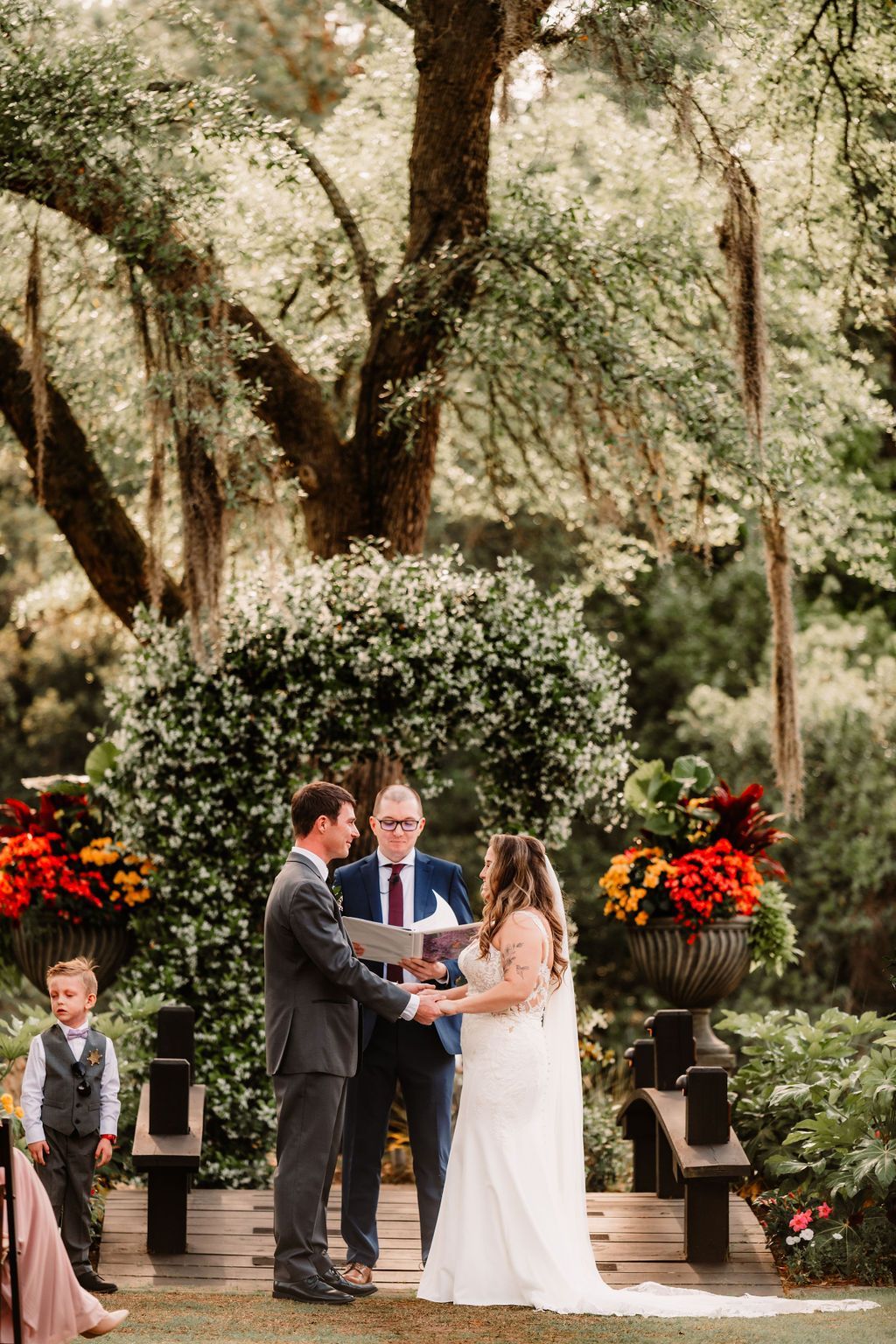 Outdoor wedding ceremony with couple exchanging vows beneath trees and floral arrangements