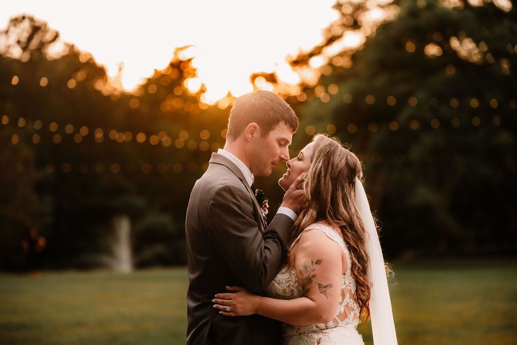 Couple embracing outdoors at sunset, with warm string lights in the background