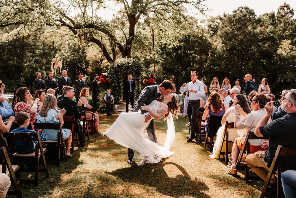 Bride and groom dance outdoors at a garden wedding ceremony, guests seated around them.