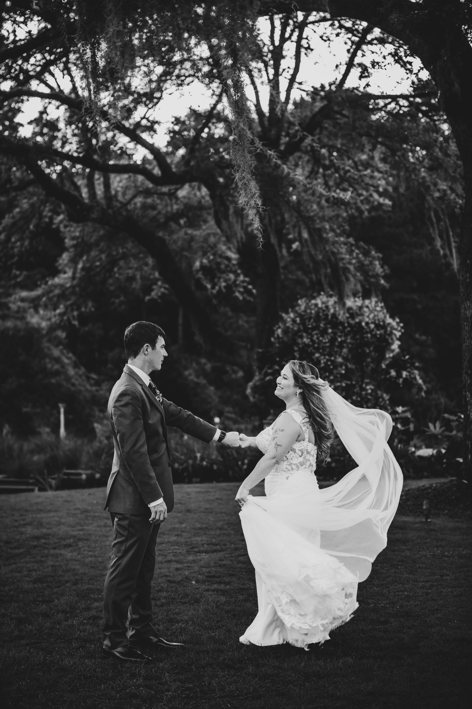 Bride and groom holding hands outdoors, the bride’s veil flowing in a dark garden.