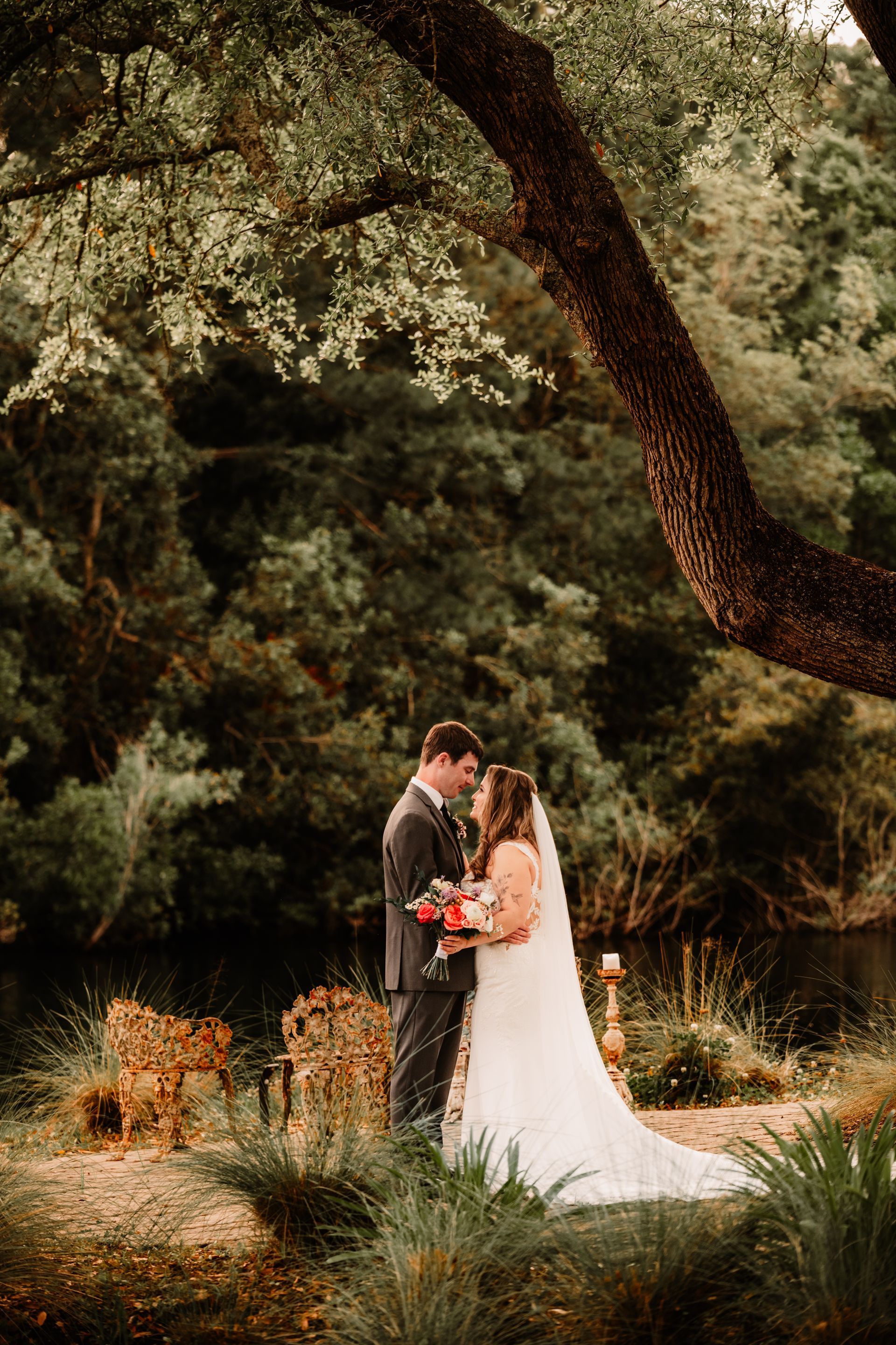 Couple exchanging vows under a large tree in a garden, bride in white dress holding a bouquet