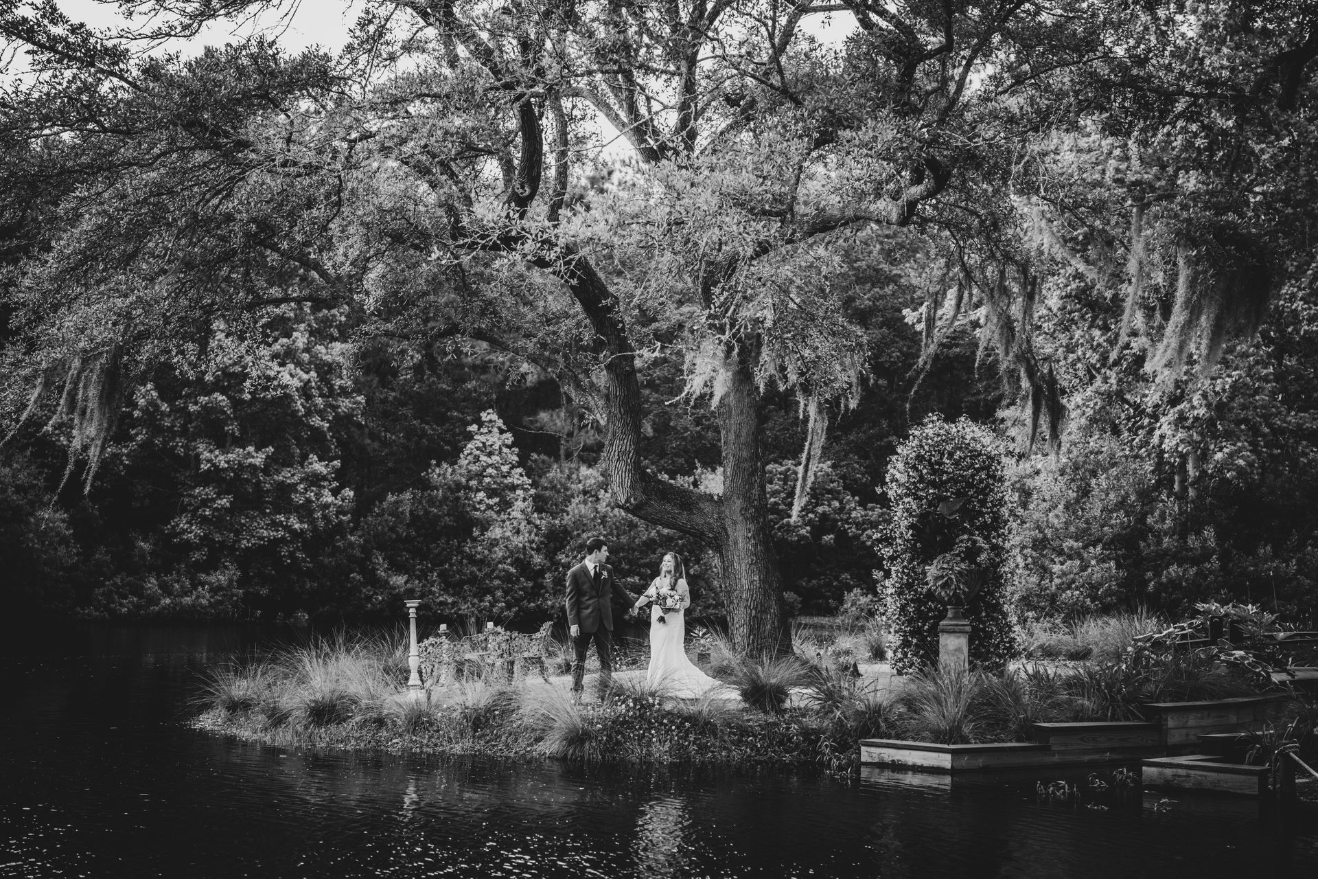 Black-and-white garden scene with a statue by a pond, surrounded by dense trees and foliage