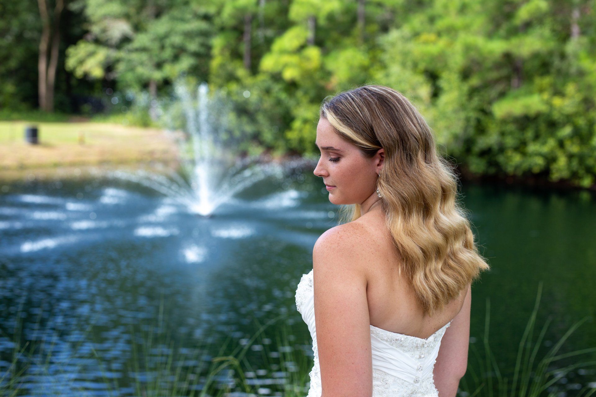 Woman in a white dress looking over a pond with a fountain in a park