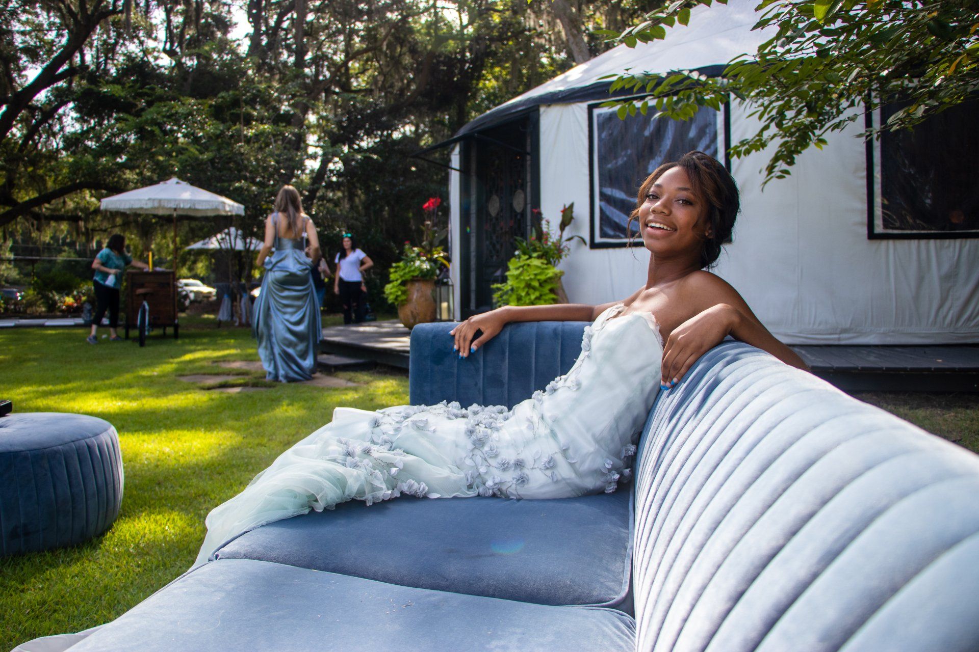 Woman in a white dress reclining on a blue outdoor sofa in a garden lounge area