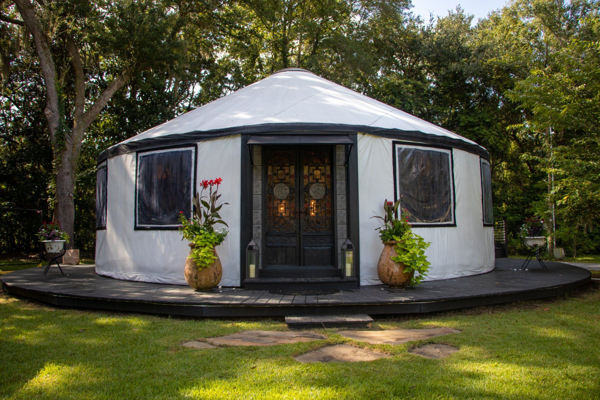 Round white cottage with dark windows and double doors, surrounded by trees and lawn
