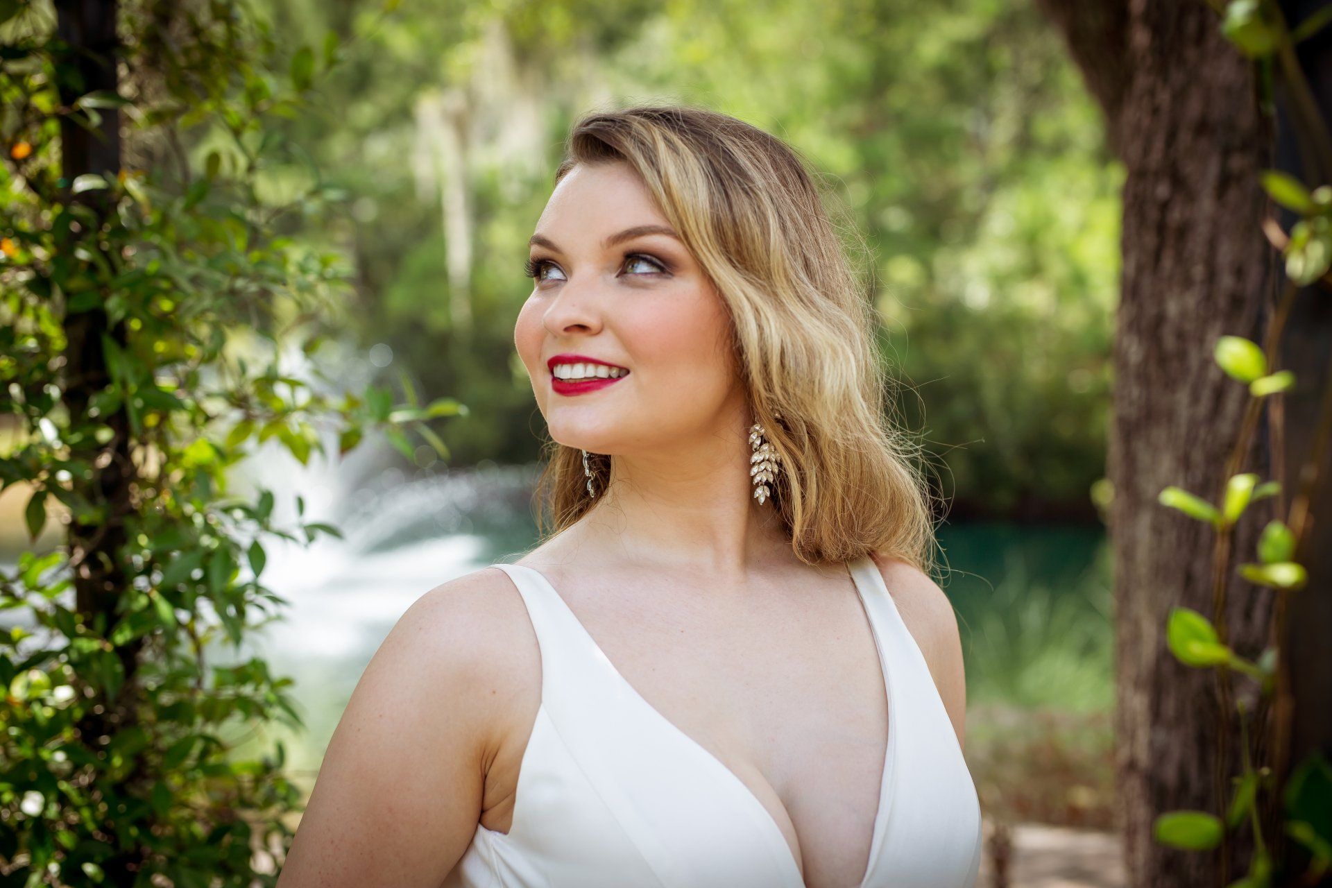 Smiling woman in a white dress standing among trees outdoors
