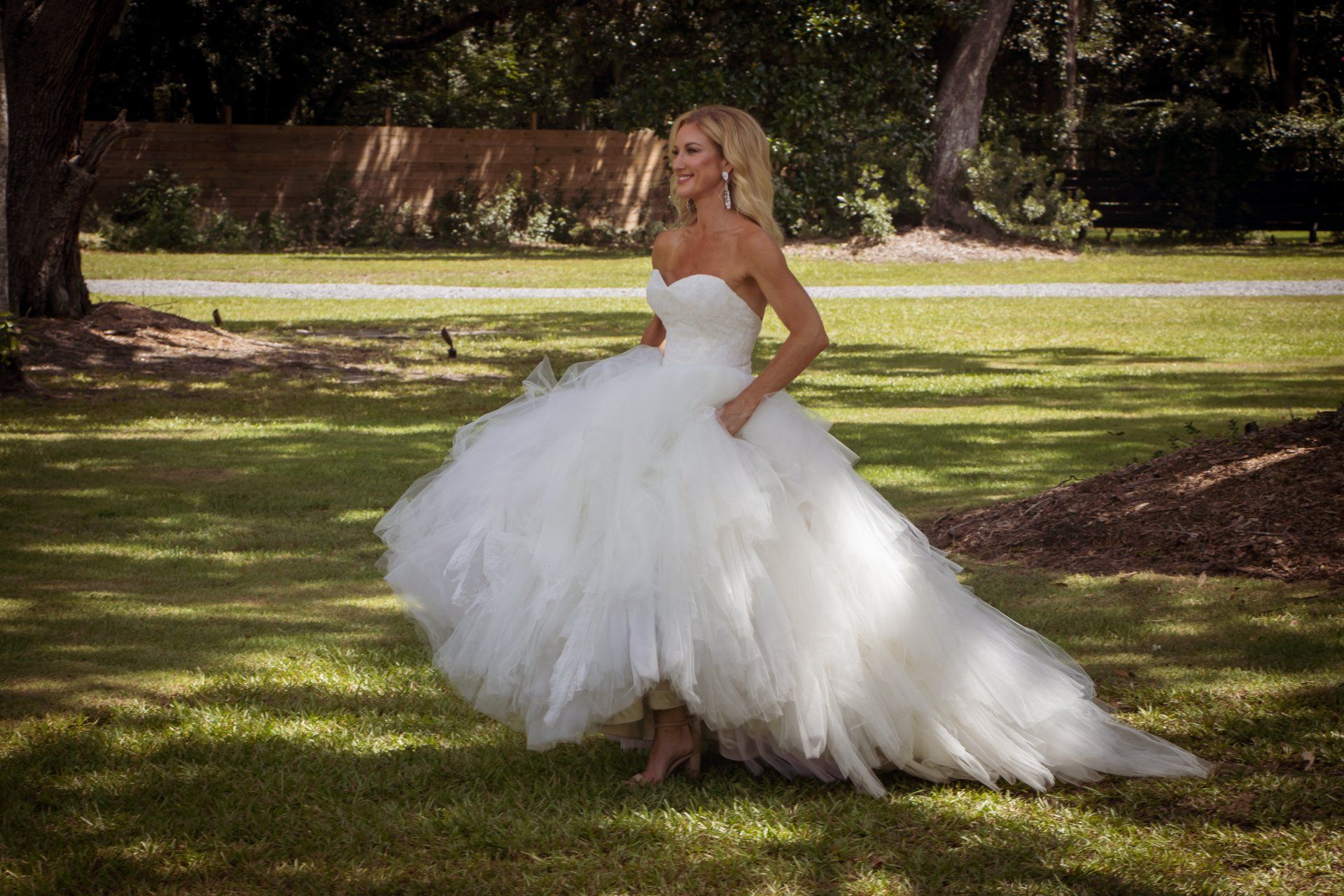 Woman in a white wedding dress standing on grass in a sunlit park