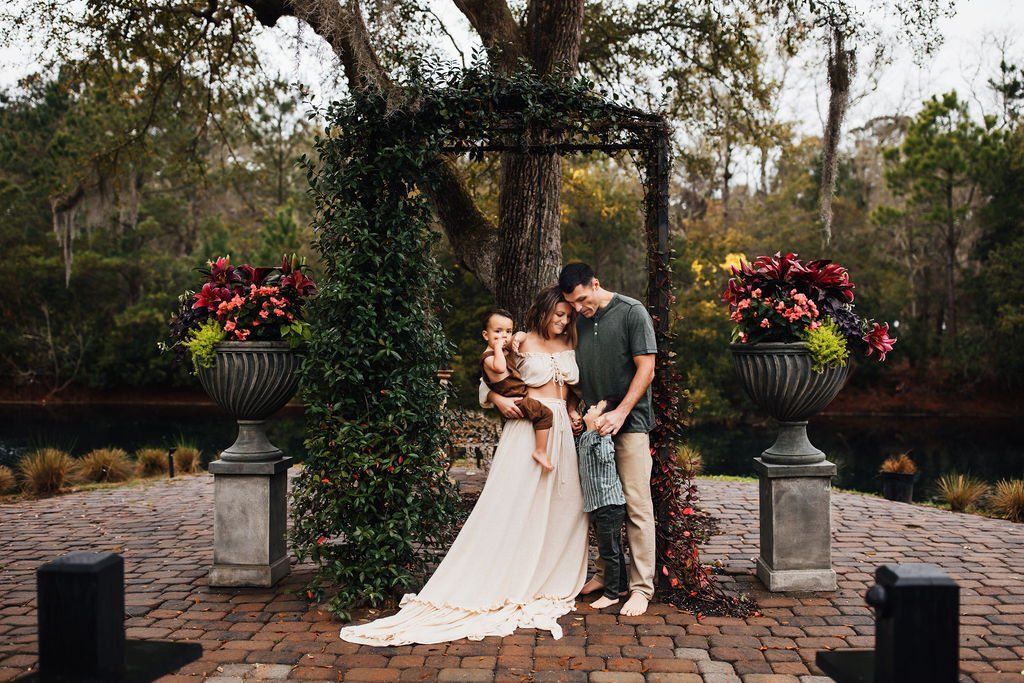 Couple in wedding attire standing under a floral arch in a garden courtyard, holding each other affectionately.