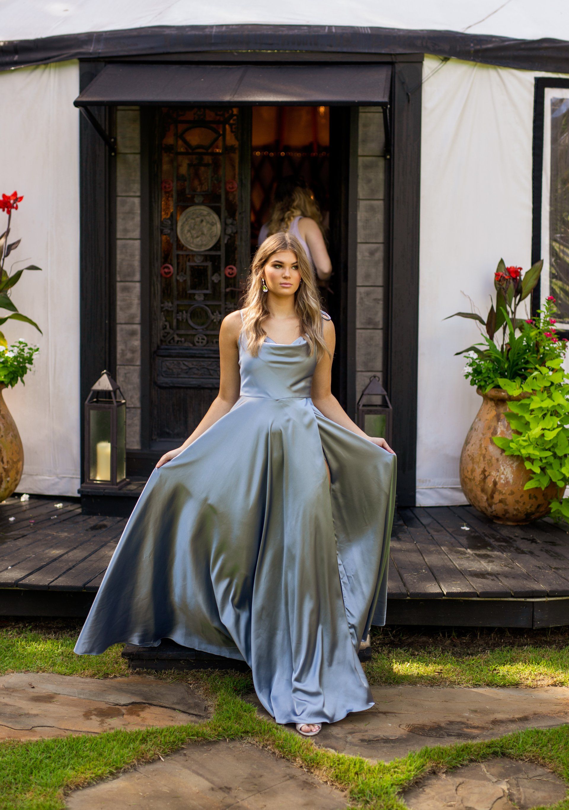 Woman in a silver gown standing on a porch outside a small house garden