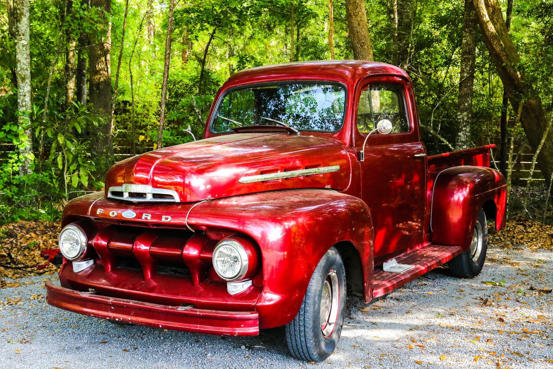 Shiny red vintage pickup truck parked on gravel in a wooded area