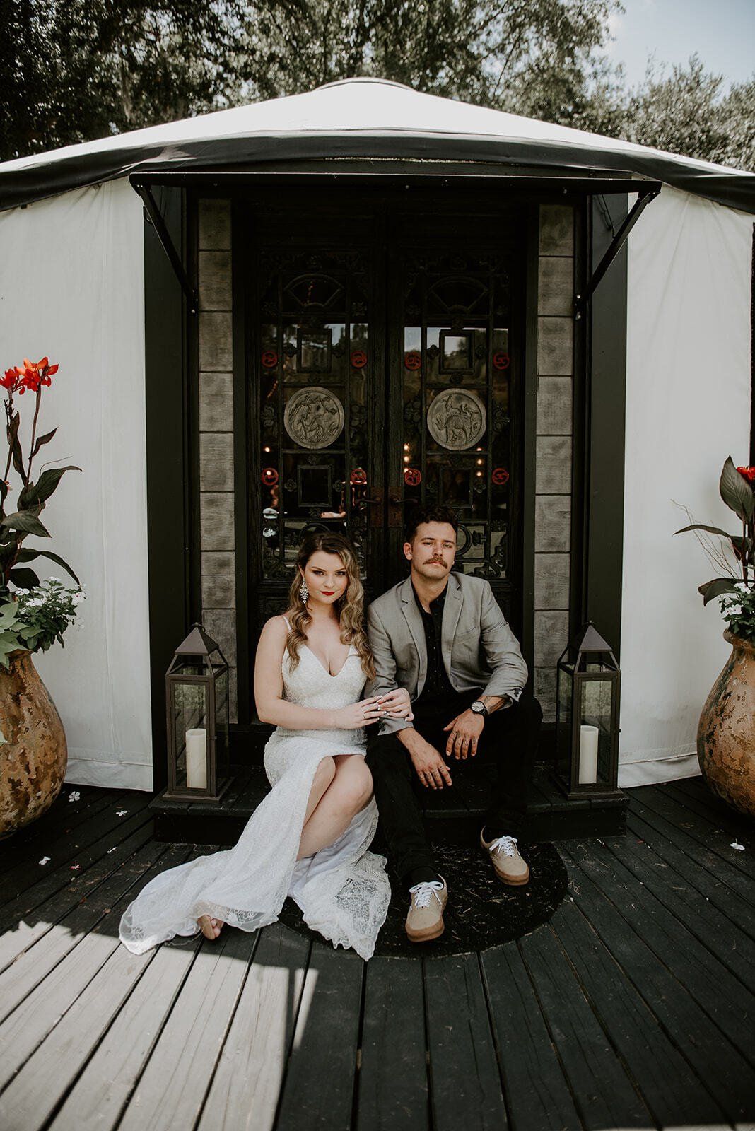 Bride and groom seated outside a small white chapel, posing on the porch with floral decor.