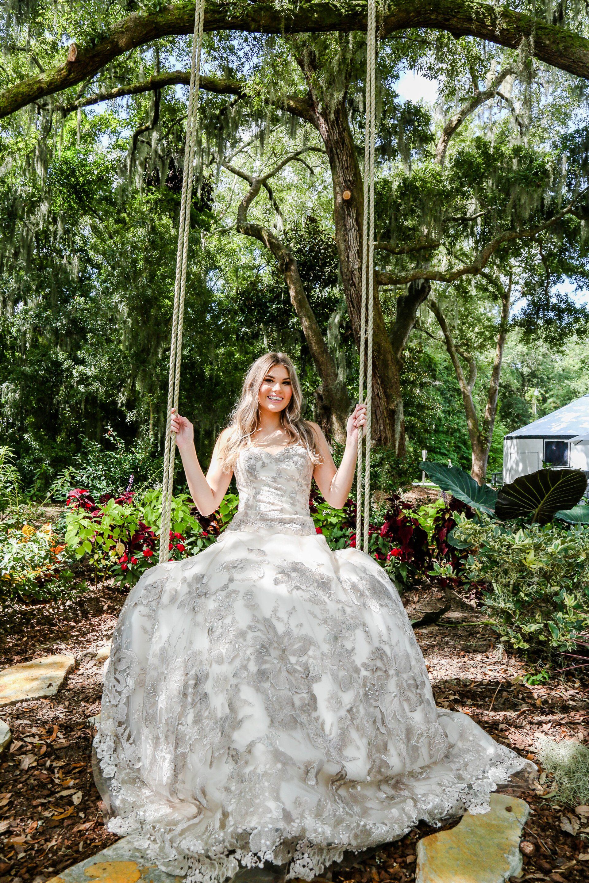 Woman in a white lace gown on a garden swing beneath an arbor of greenery