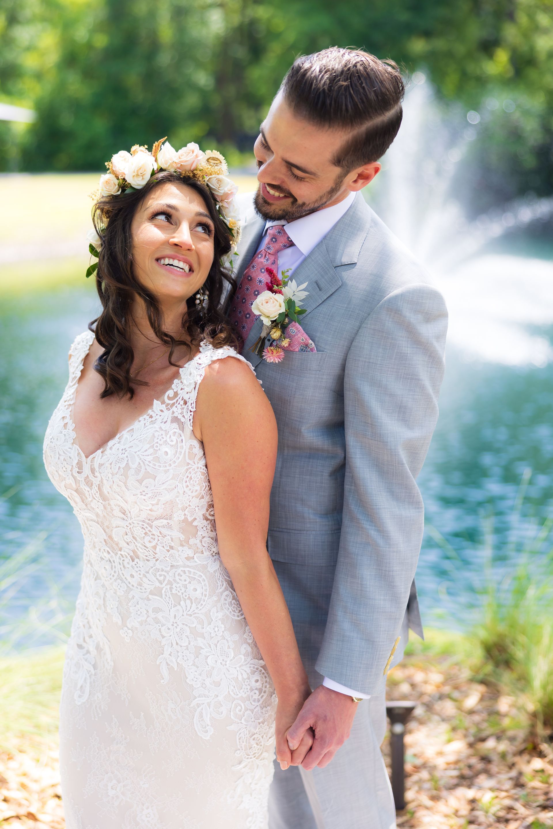 Bride and groom smiling by a fountain, dressed for a wedding outdoors