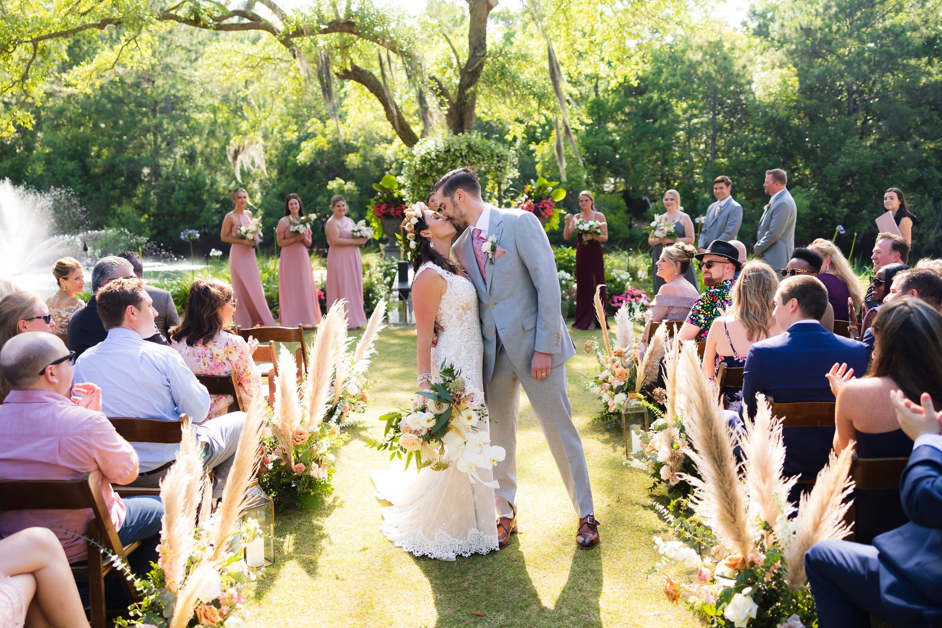 Bride and groom kiss at an outdoor garden wedding ceremony with guests seated nearby.