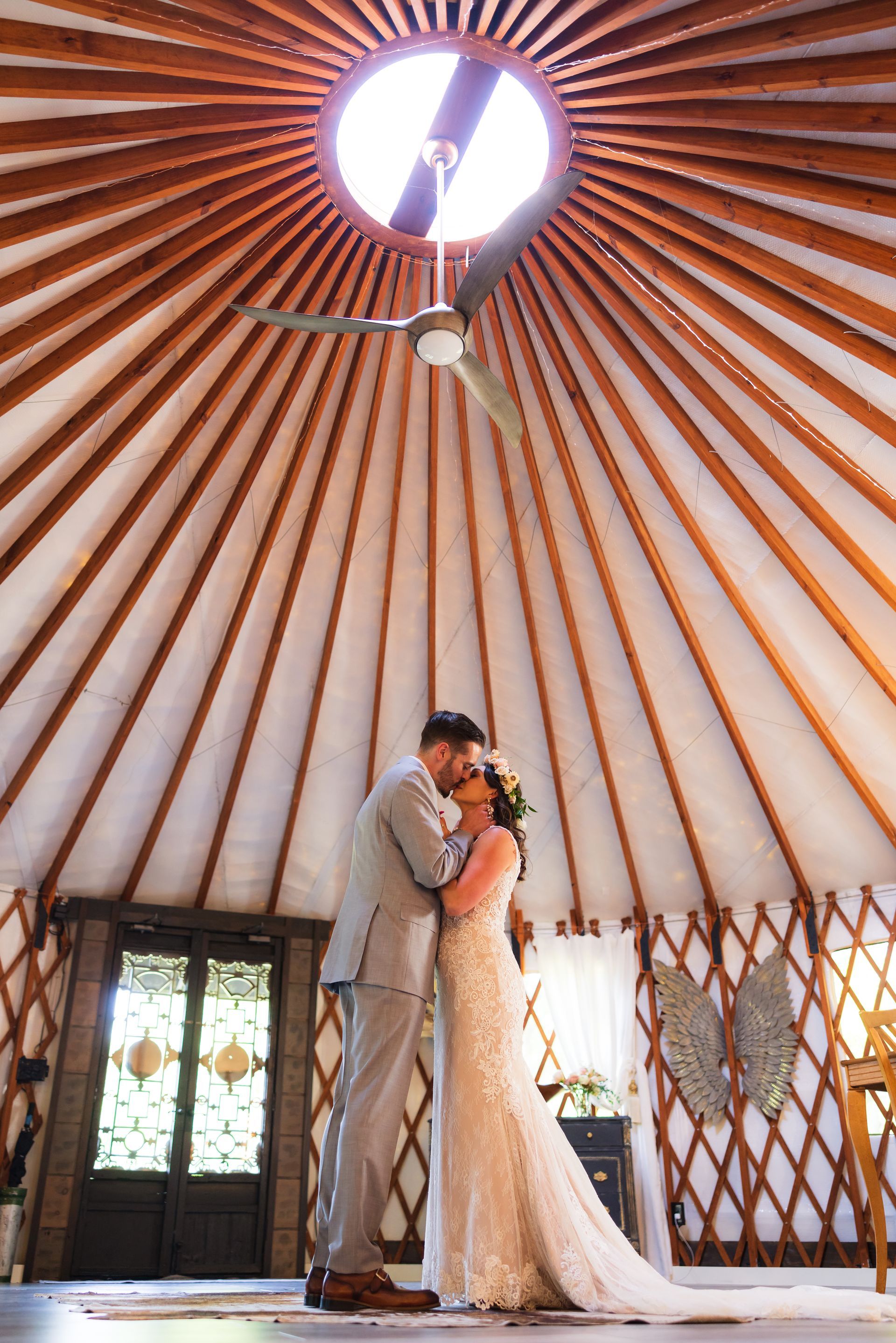 Couple embracing in a sunlit yurt-like venue, with a circular skylight above and patterned walls around them