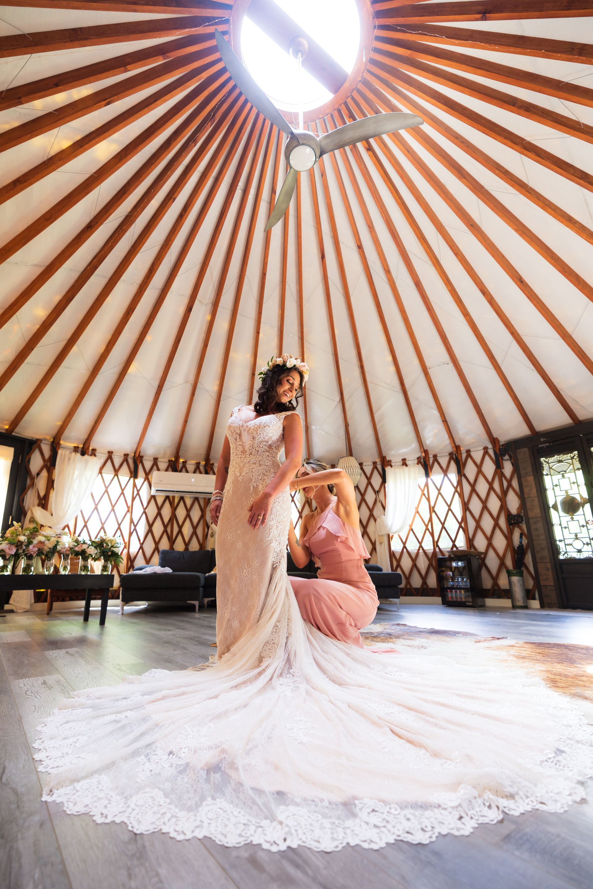 Bride in lace gown under a circular pavilion, with a bridesmaid behind her and light streaming from above