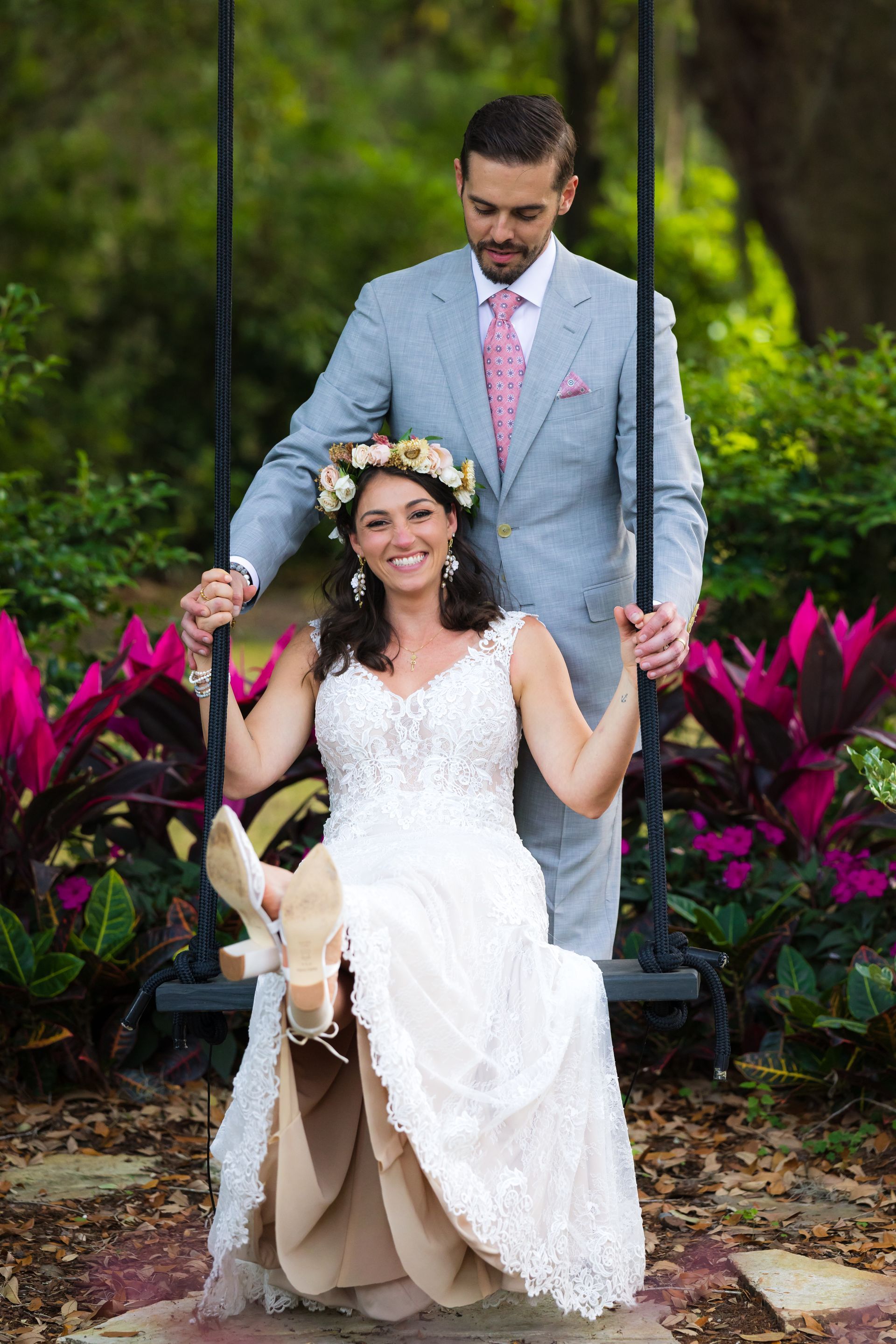 Bride and groom on a swing in a garden, surrounded by bright pink flowers and greenery