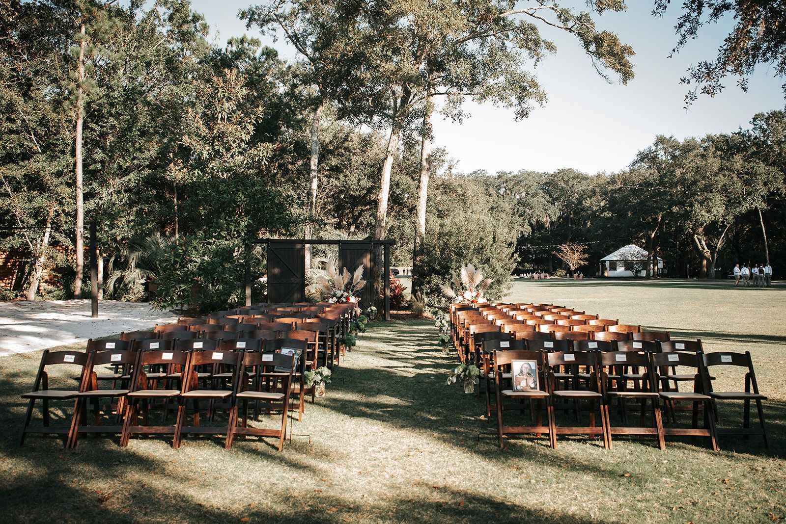 Outdoor wedding ceremony setup with rows of wooden chairs facing an arch under trees on a grassy lawn