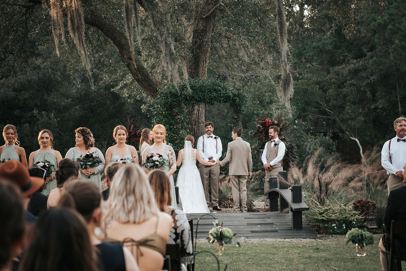 Outdoor wedding ceremony with bride, groom, and wedding party standing in front of trees
