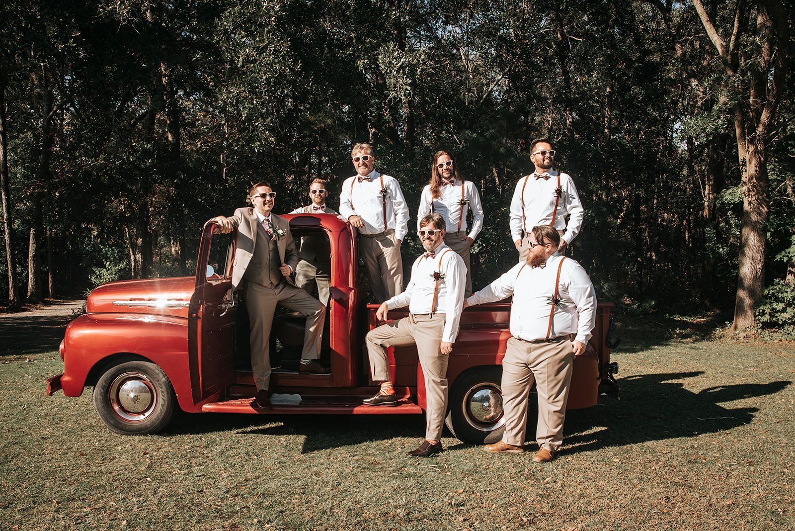 Five people posing beside a red vintage pickup truck in a wooded outdoor setting