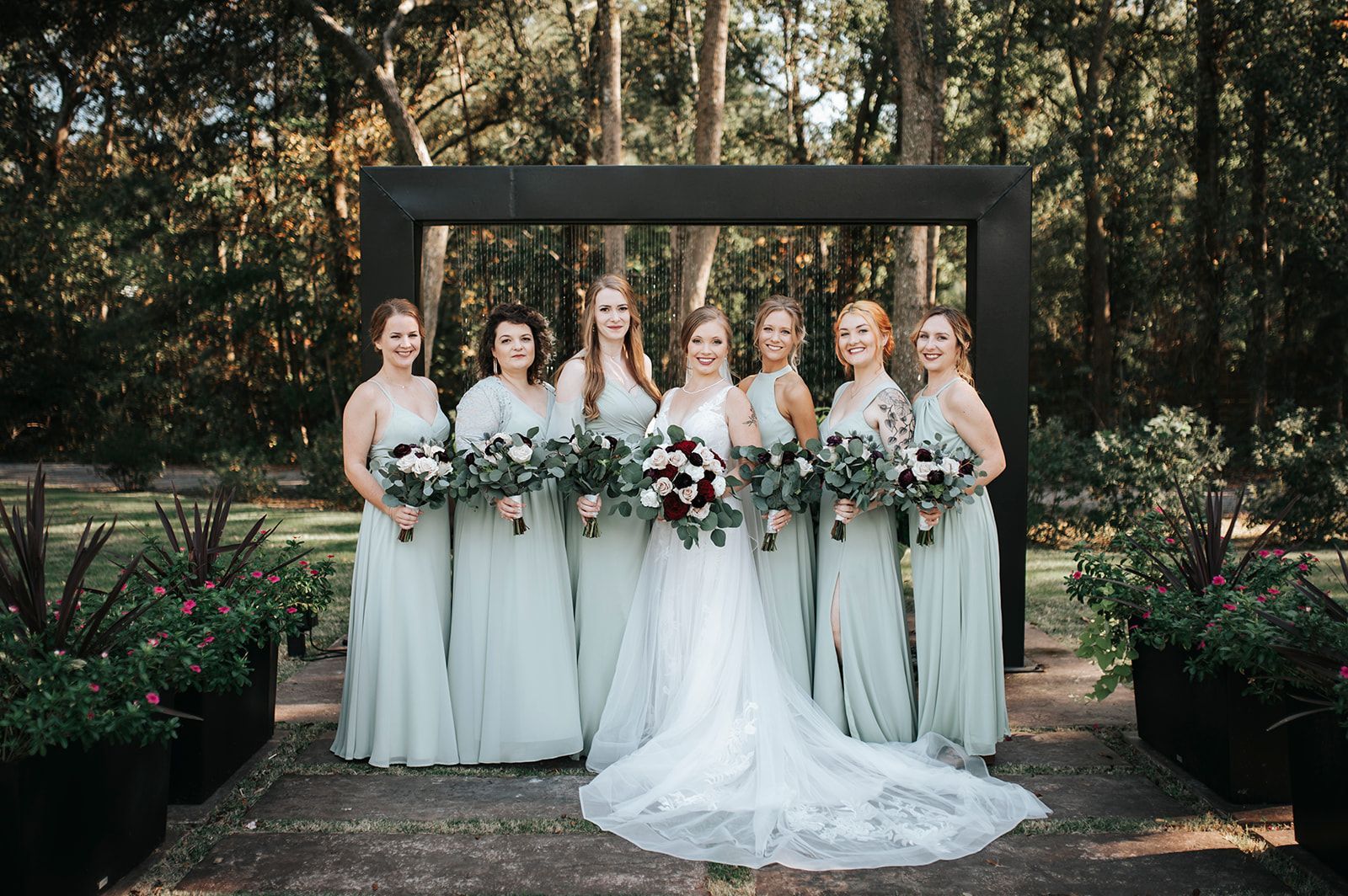 Bridesmaids and bride in white dresses holding bouquets in a garden wedding setting.