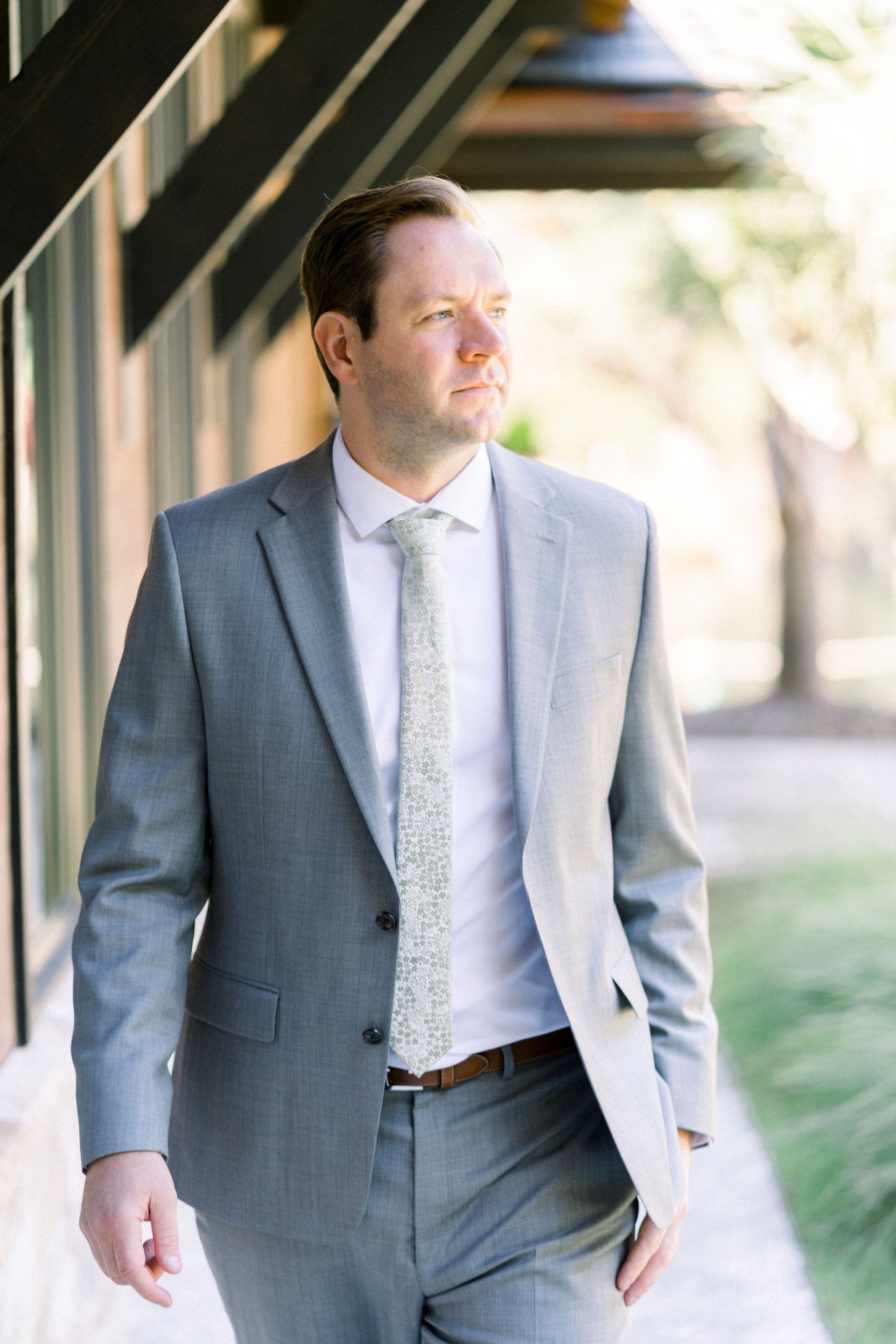 Man in a light gray suit walking outdoors beside a columned walkway