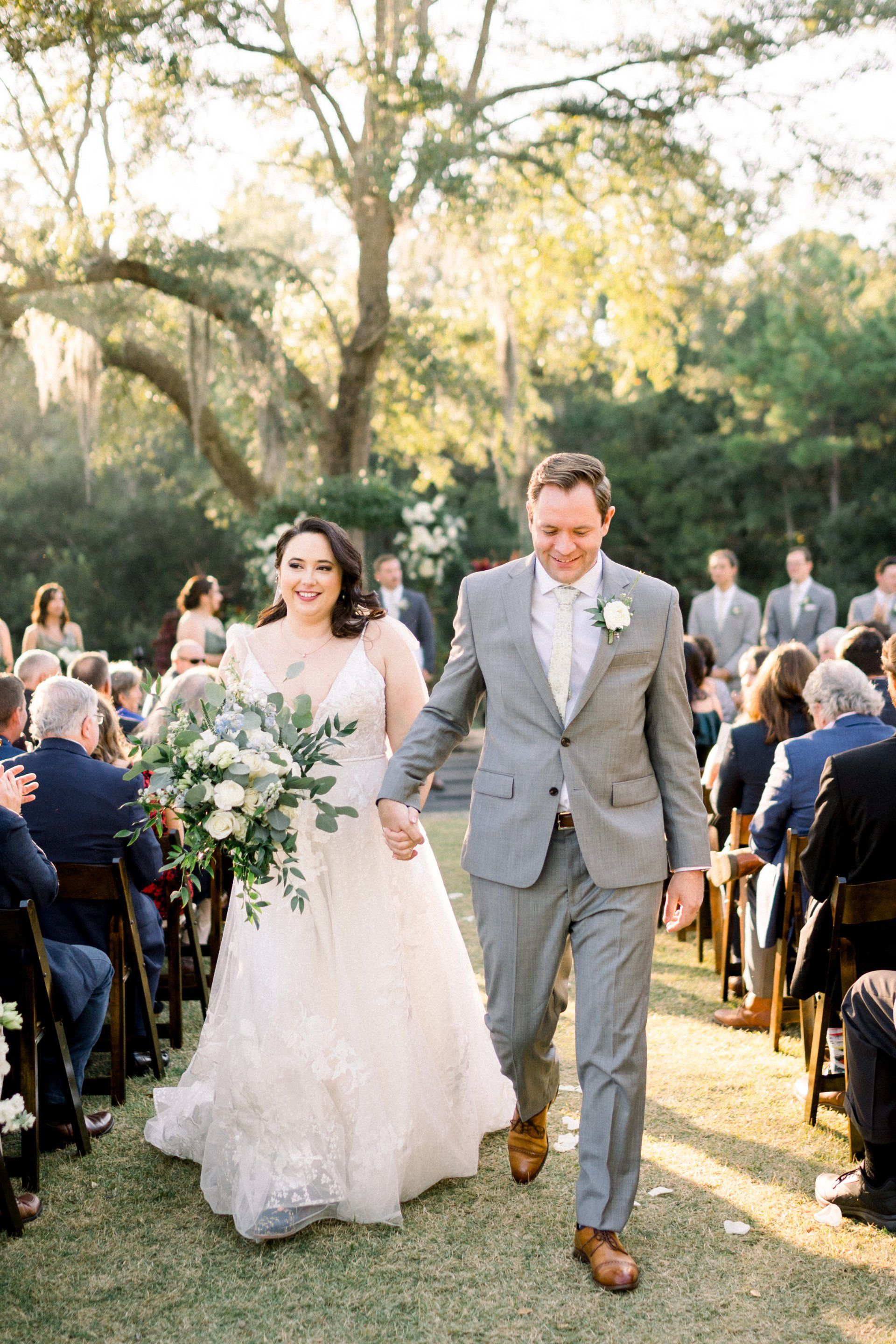 Bride and groom walking down an outdoor aisle at a garden wedding, guests seated nearby.