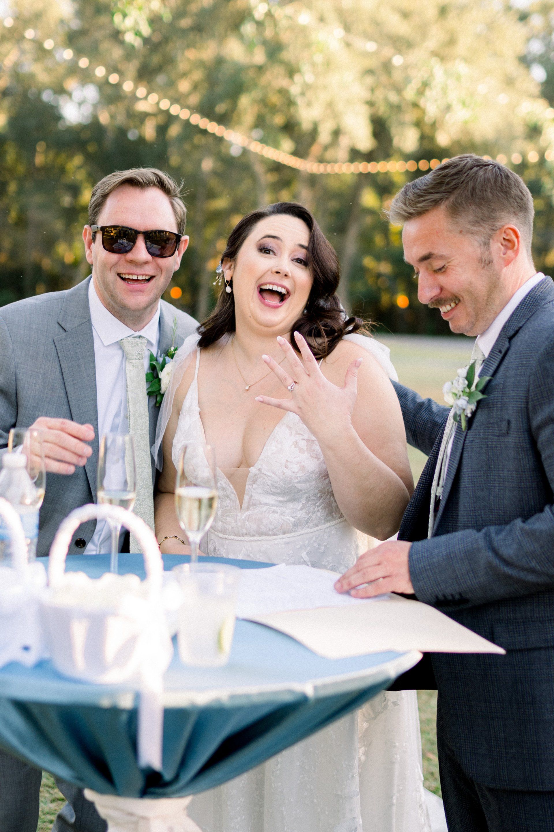 Wedding guests celebrating outdoors at a table, smiling and laughing in formal attire