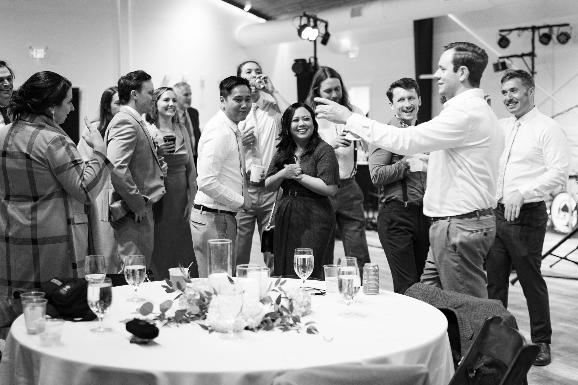 People mingling at a reception, with a man holding up a drink in a lively indoor event scene.