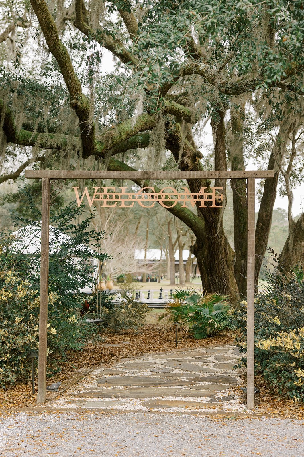 Stone path under a wooden archway in a wooded garden with tall trees and hanging moss