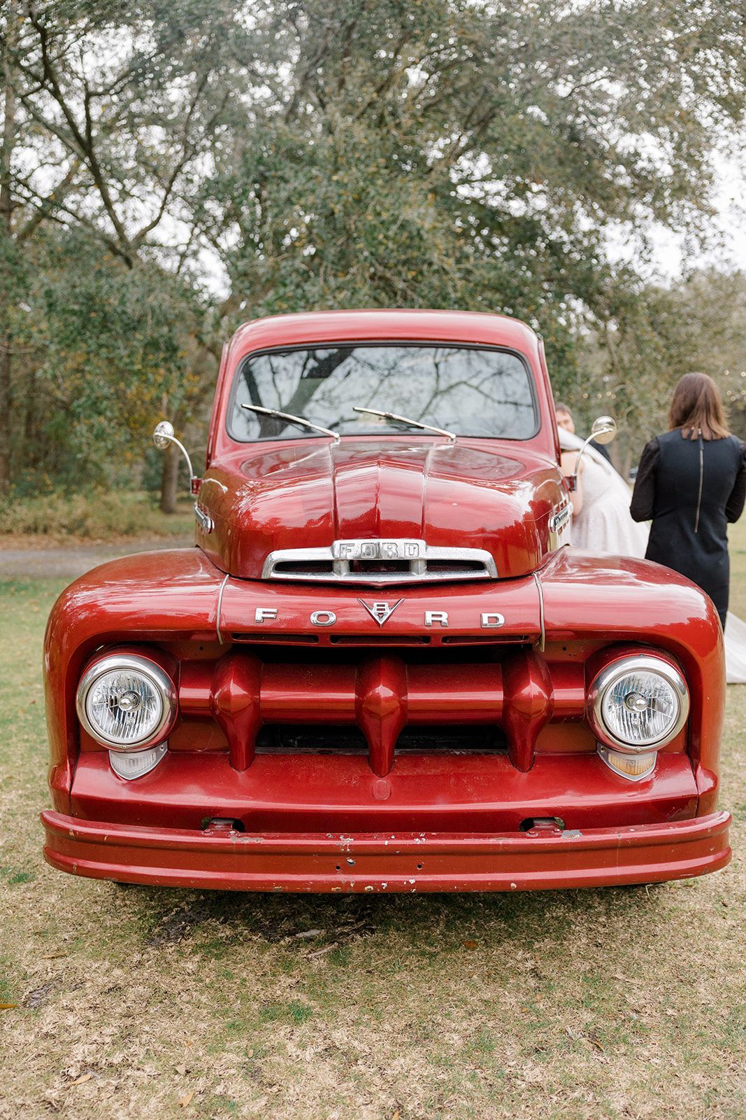 Front view of a red vintage Dodge truck parked on grass, with a person standing beside it