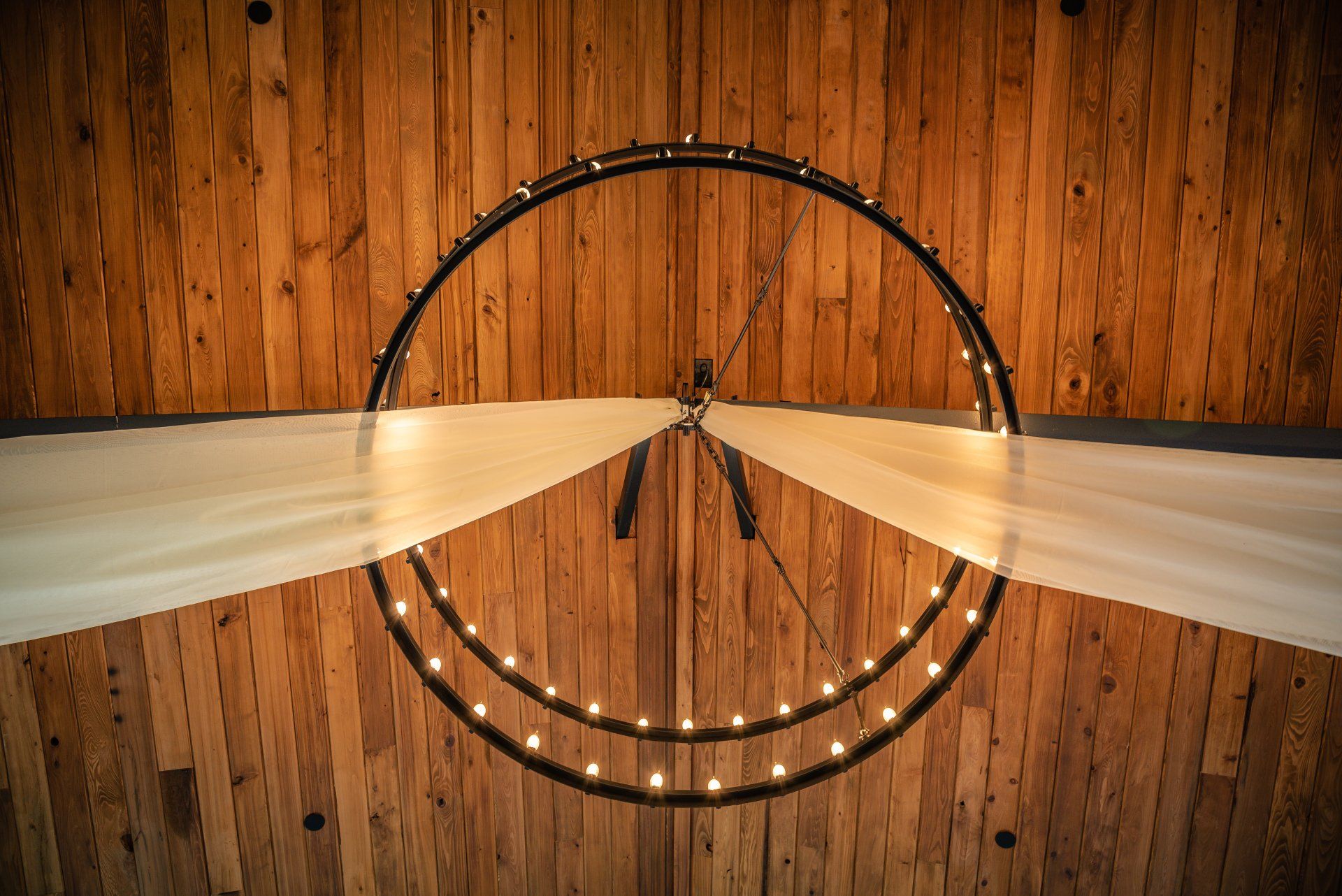 Wooden ceiling with a circular chandelier and flowing white drapes