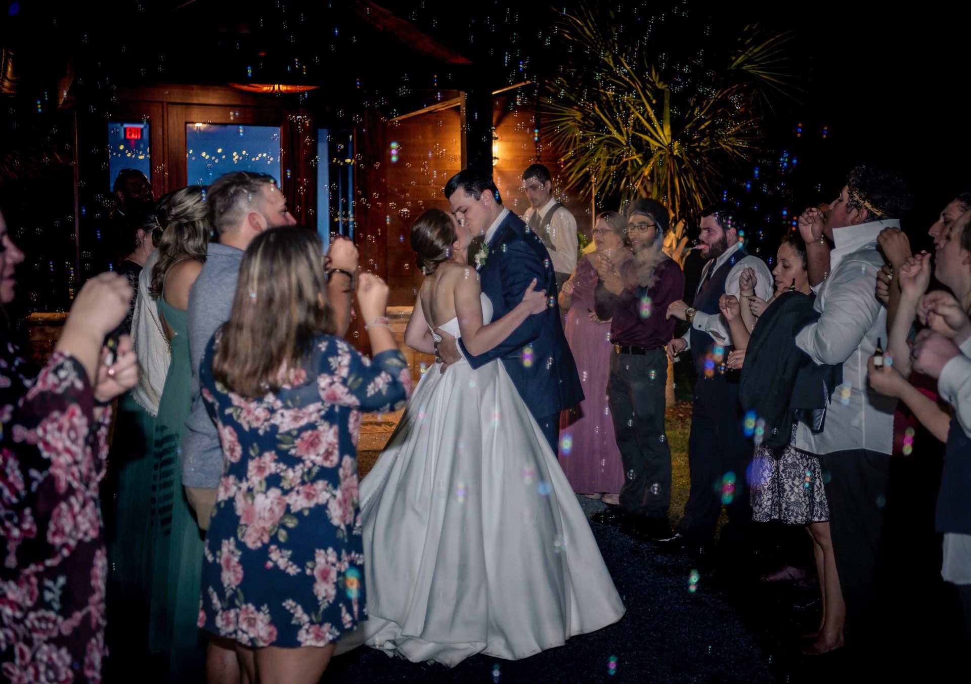 Couple dancing in a dimly lit party, surrounded by guests, with sparkling lights in the background