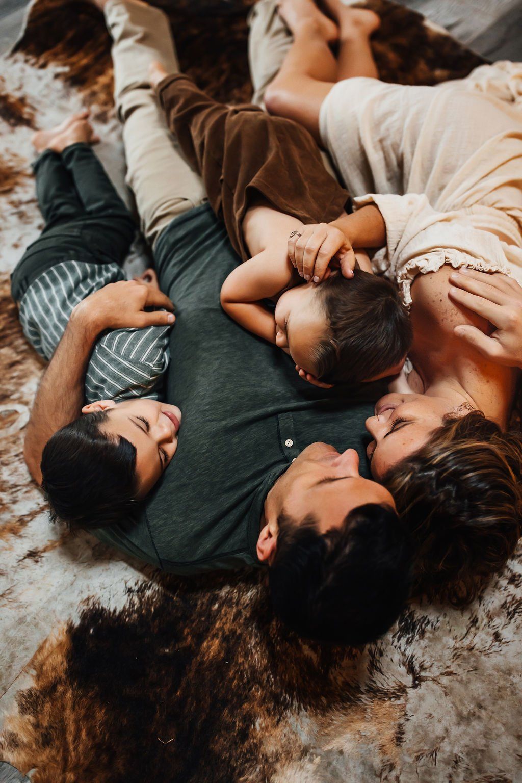 Four people lying in a circle on a textured floor, holding hands in a close group hug.