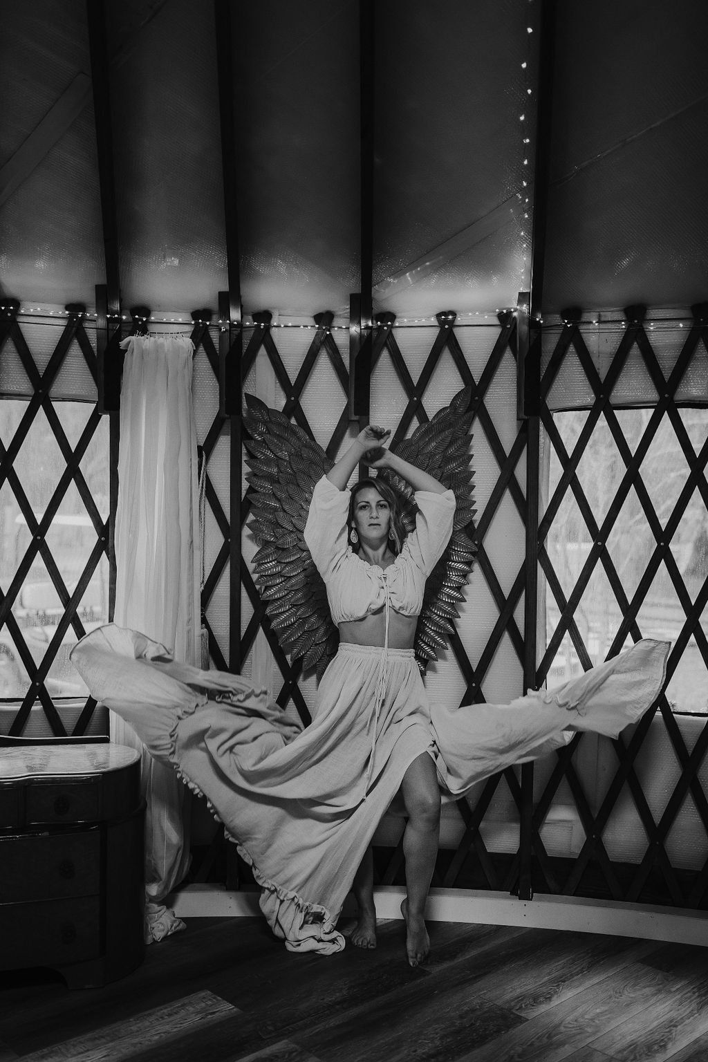 Woman in a flowing dress posing with arms raised inside a patterned tent-like backdrop.