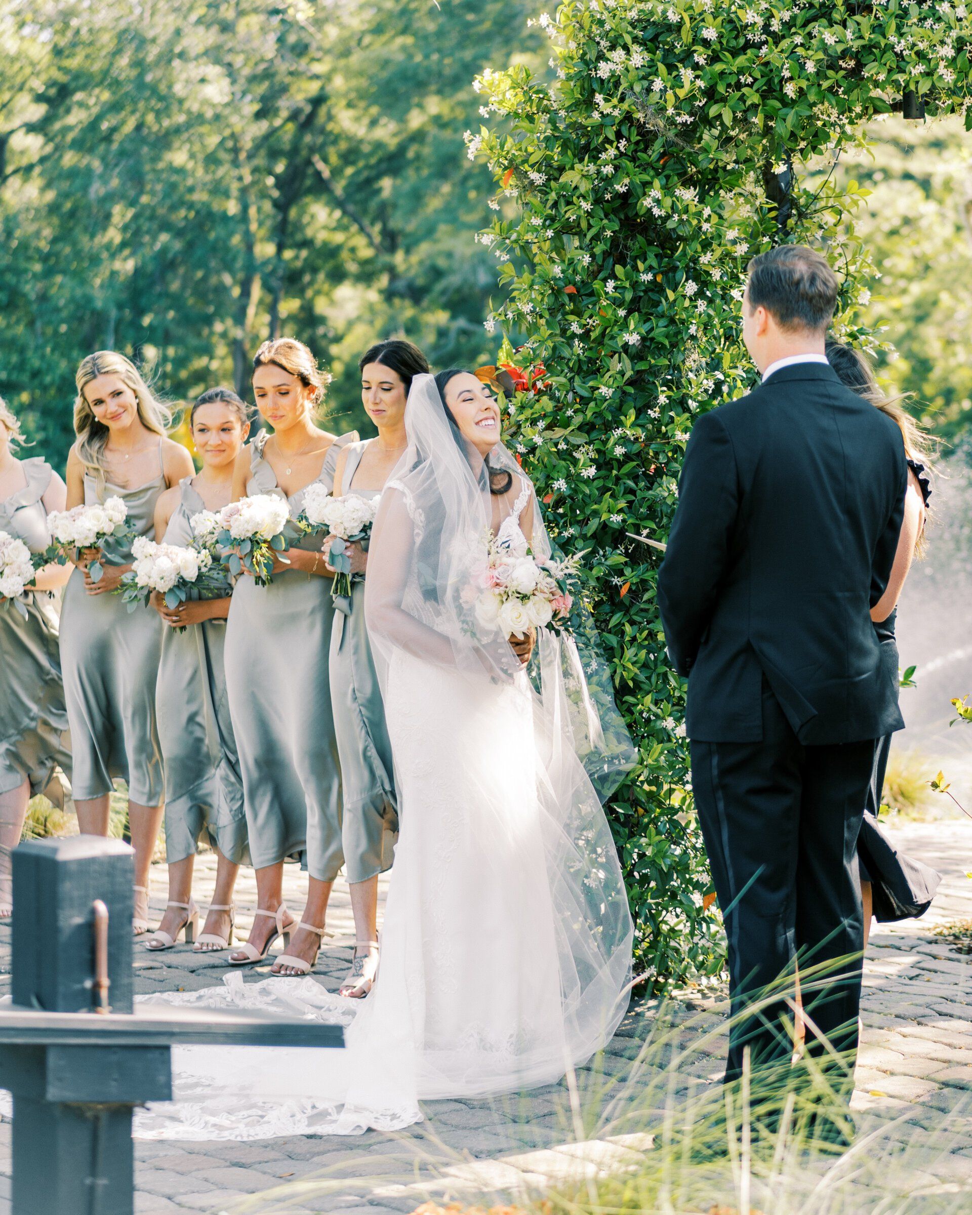 Bride and groom standing outdoors with bridesmaids in silver dresses and white bouquets
