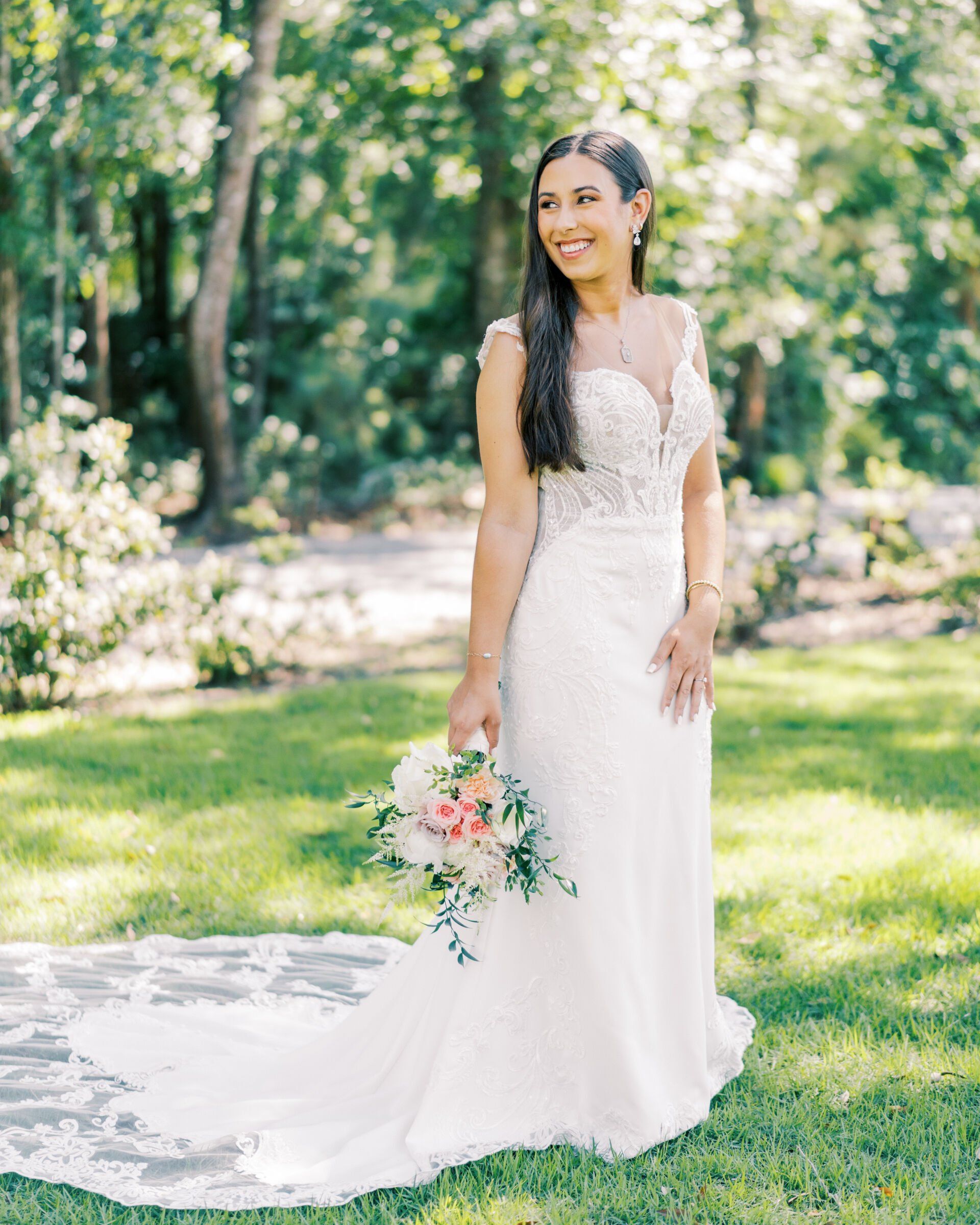 Bride in a white lace gown holding a pastel bouquet in a sunlit garden