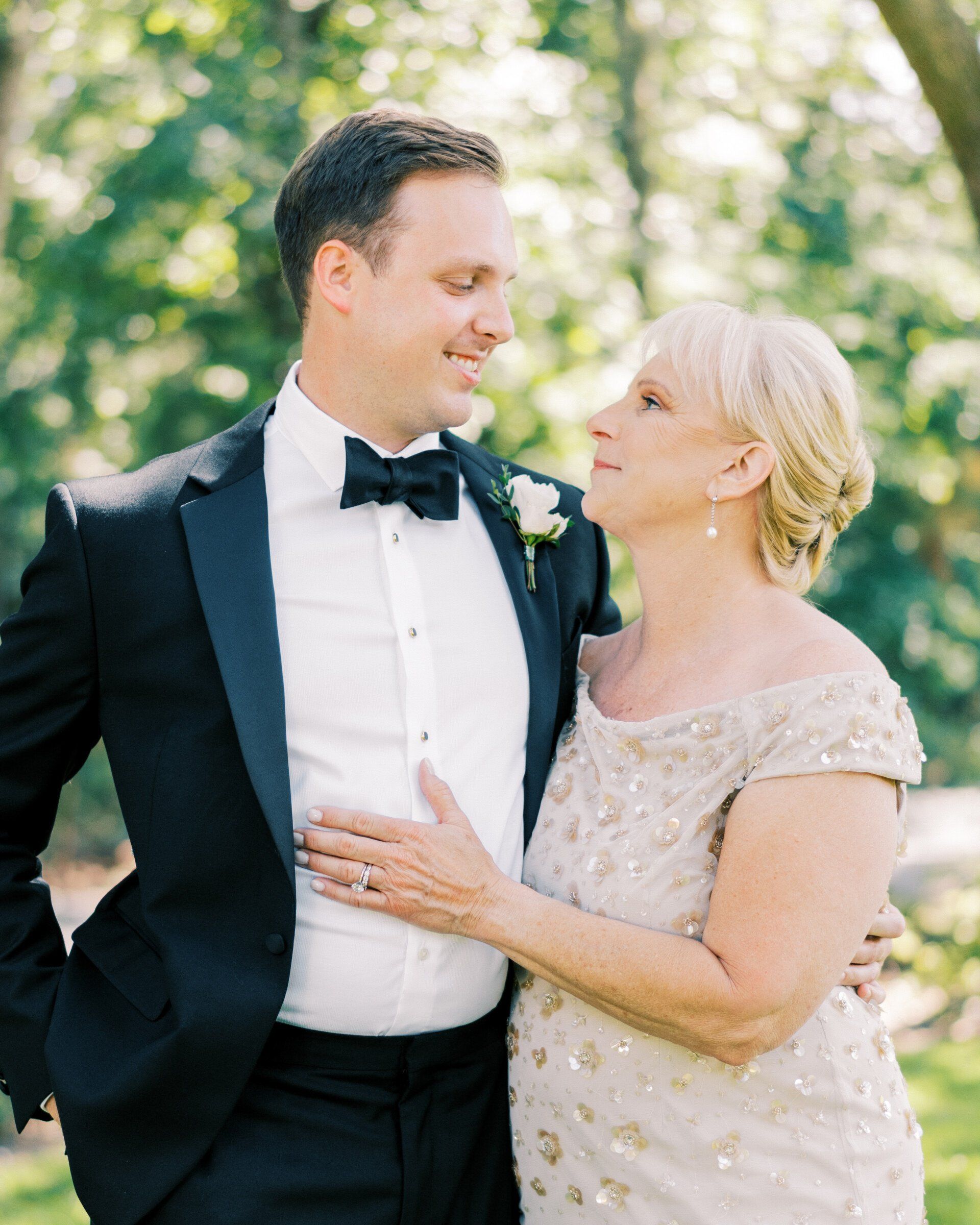 Smiling couple in wedding attire outdoors, gazing at each other in soft sunlight.