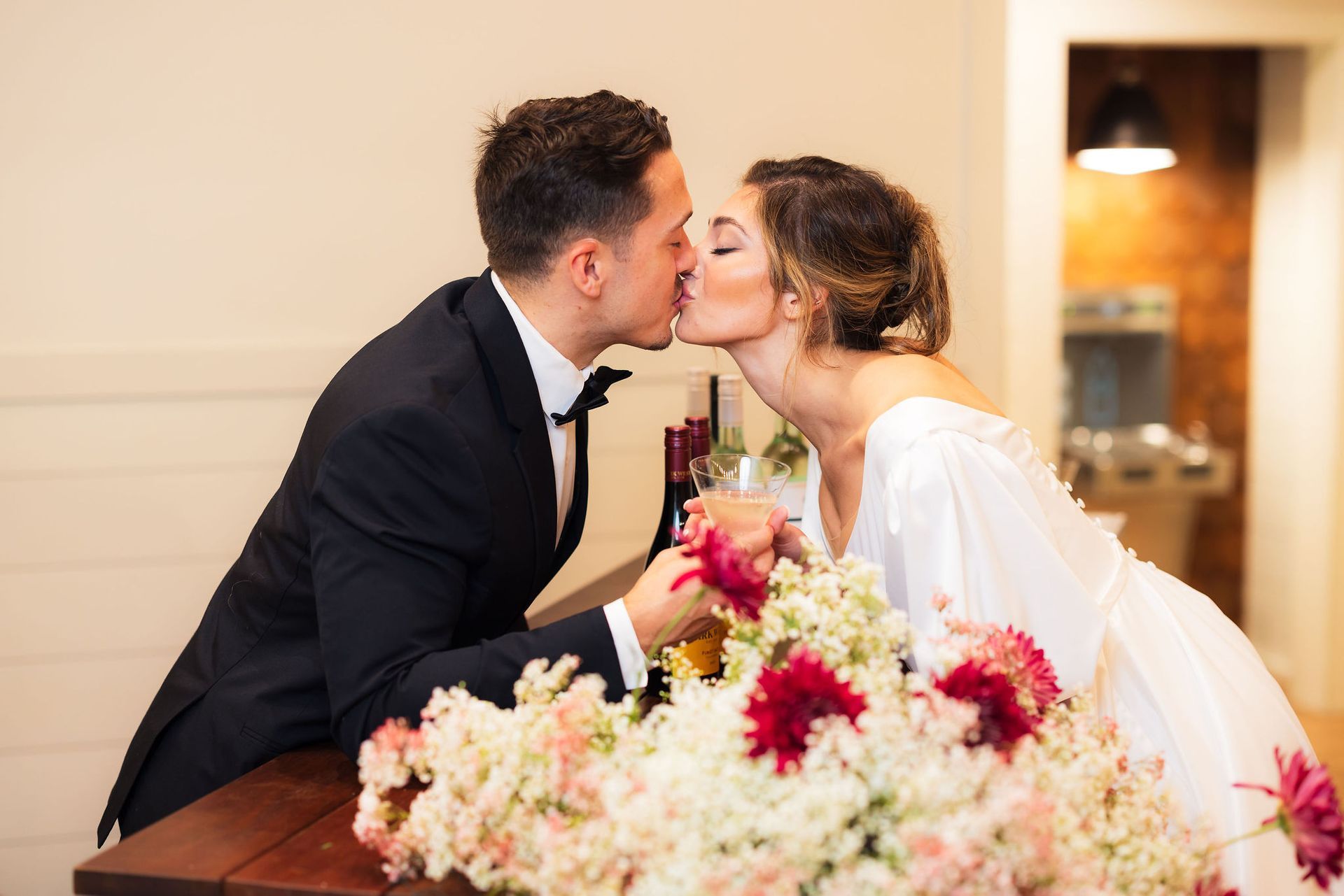 Couple kissing at a wedding, with a bouquet of pink and white flowers in the foreground